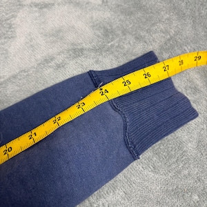 May include: Close-up of a blue fabric sleeve with a yellow measuring tape. The tape shows measurements from 20 to 29 inches. The fabric appears to be a sweatshirt material.
