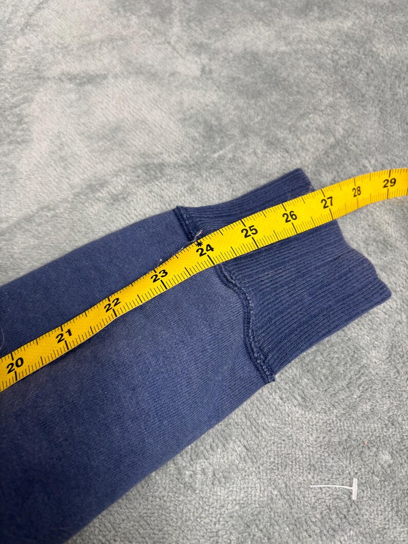 May include: Close-up of a blue fabric sleeve with a yellow measuring tape. The tape shows measurements from 20 to 29 inches. The fabric appears to be a sweatshirt material.