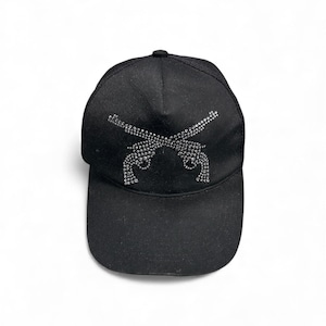 May include: Black baseball cap featuring a rhinestone design of two crossed pistols. The cap has a curved brim and a mesh back. The design is made of small, sparkling rhinestones.