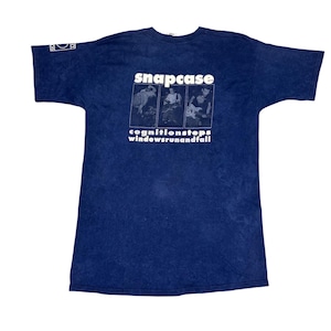 May include: A navy blue t-shirt with the band name "snapcase" in white block letters. Below the band name are three black and white images of band members. The text "cognitionstops windowsrunandfall" is printed below the images.