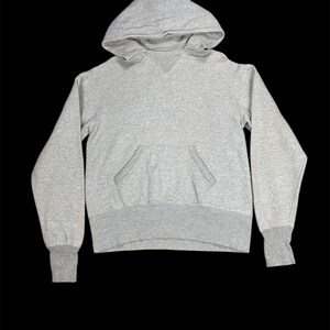 Può includere: Una felpa con cappuccio grigio mélange con cappuccio con coulisse e tasca a marsupio. La felpa a maniche lunghe ha polsini e orlo a coste. La felpa con cappuccio è realizzata in un materiale morbido e confortevole.