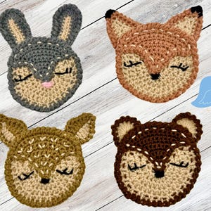 Può includere: Quattro volti di animali all'uncinetto con gli occhi chiusi. Gli animali sono una volpe, un cervo, un coniglio e un procione. I volti sono tutti beige con accenti marroni.