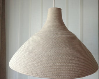 May include: A beige woven pendant light fixture with a wide, rounded shade hangs from a white cord and a wooden ceiling mount.