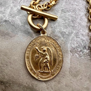 Pu&ograve; includere: Collana color oro con un ciondolo rotondo raffigurante un angelo. Il ciondolo &egrave; attaccato a una catena d'oro con una chiusura a levetta. La collana &egrave; un accessorio religioso o spirituale.