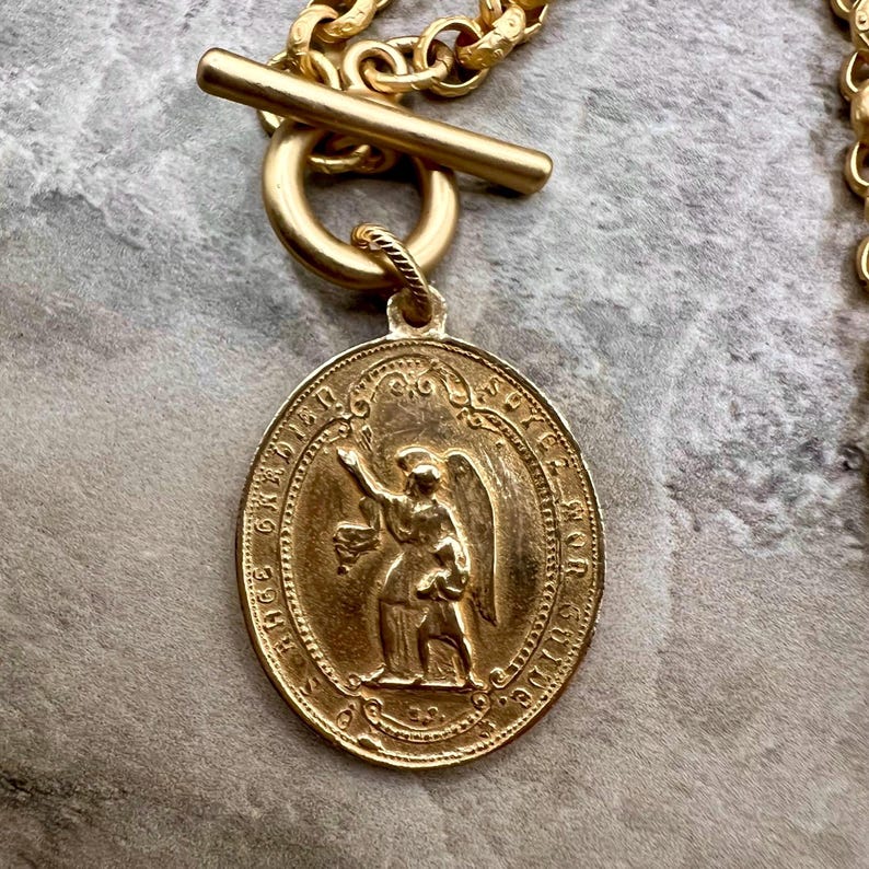 Pu&ograve; includere: Collana color oro con un ciondolo rotondo raffigurante un angelo. Il ciondolo &egrave; attaccato a una catena d'oro con una chiusura a levetta. La collana &egrave; un accessorio religioso o spirituale.