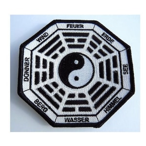 May include: A black and white embroidered patch featuring a yin yang symbol at its centre. The patch is enclosed in an octagon with the words "Feuer", "Wind", "Donner", "Berg", "Wasser", "Himmel", "See", and "Erde" written around the perimeter.