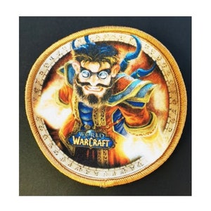 Könnte beinhalten: Runder Aufnäher mit einer Cartoon-Figur aus World of Warcraft. Die Figur hat einen Bart, eine Brille und blaue Hörner. Der Aufnäher hat einen goldenen Rand und die Worte "World of Warcraft" sind aufgedruckt.