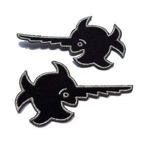 Puede incluir: Dos parches bordados negros en forma de pez espada para planchar. Los parches tienen un contorno plateado.