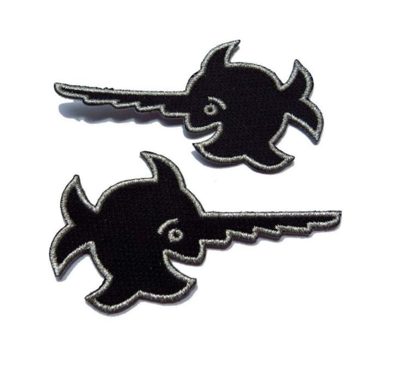 Puede incluir: Dos parches bordados negros en forma de pez espada para planchar. Los parches tienen un contorno plateado.