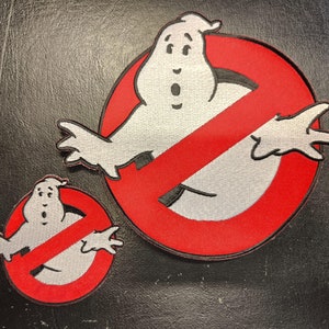 Könnte beinhalten: Zwei gestickte rote und weiße Patches mit einer Geisterfigur in einem Kreis mit einer diagonalen roten Linie. Der größere Patch hat einen Durchmesser von etwa 10 cm und der kleinere Patch einen Durchmesser von etwa 5 cm.