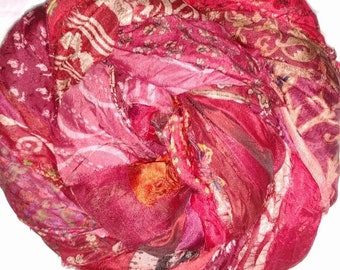 May include: A pink and red silk scarf with a paisley pattern. The scarf is made of recycled silk and is hand-woven.