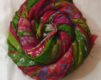 May include: A bundle of colorful fabric scraps in shades of pink, red, and green. The fabric is arranged in a circular shape, with the ends of the scraps frayed and uneven.