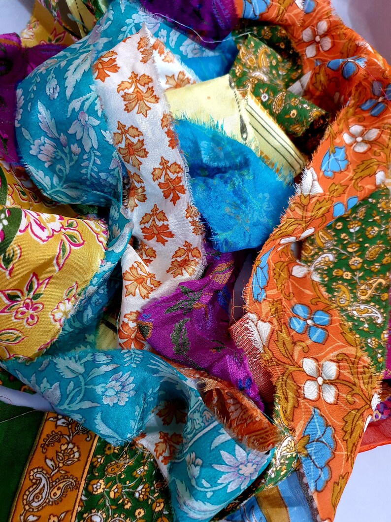 May include: A close-up of a bundle of colorful fabric scraps with floral patterns. The fabric is in shades of blue, green, orange, yellow, and purple.