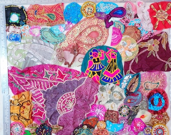 May include: A collection of colorful fabric patches with intricate embroidery and beadwork. The patches feature various shapes, including floral designs, paisleys, and abstract patterns. Colors include pink, blue, gold, and green. A ruler is visible along the left side.