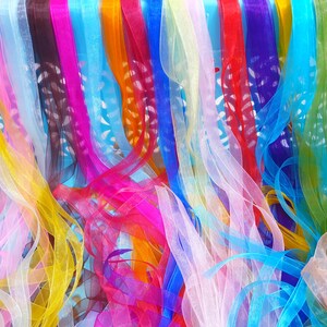 May include: A close-up of a collection of colourful ribbons in various shades, including pink, yellow, orange, red, blue, and green. The ribbons are made of a sheer material, creating a layered effect. The ribbons are arranged vertically, with some overlapping.