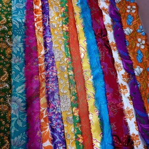 May include: A collection of colorful fabric strips with various floral and paisley patterns. The strips are arranged vertically and have a frayed edge.
