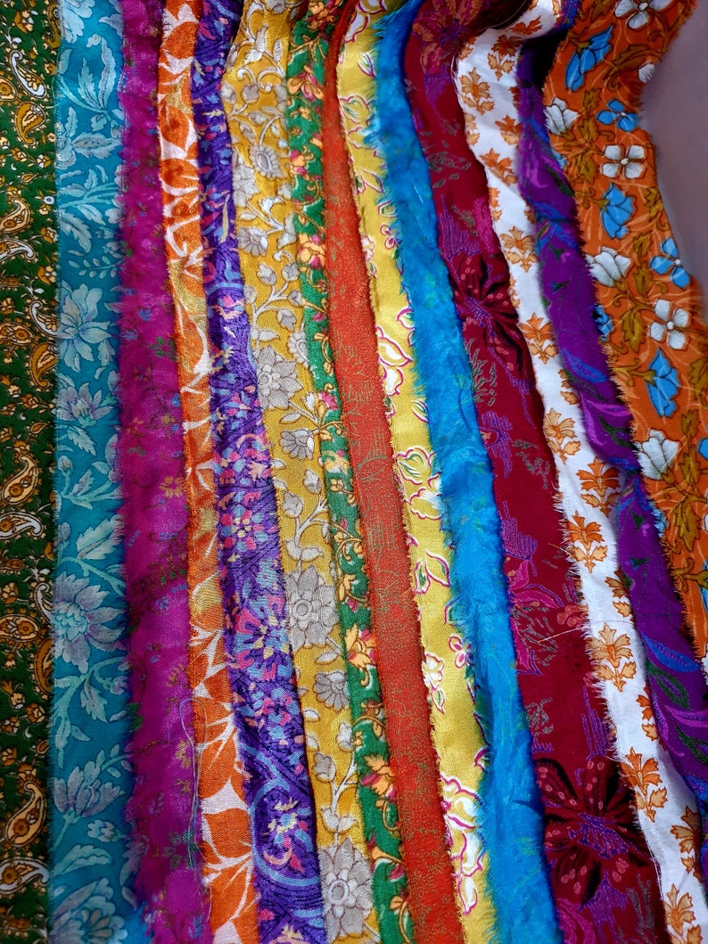 May include: A collection of colorful fabric strips with various floral and paisley patterns. The strips are arranged vertically and have a frayed edge.