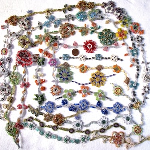 May include: A collection of beaded necklaces and bracelets in various colours and designs. The jewellery features intricate floral patterns and geometric shapes, with beads in shades of blue, green, red, yellow, and silver.