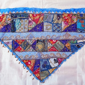 May include: A triangular patchwork quilt with a blue border and a white background. The quilt is made of various fabrics in different colors and patterns, including red, green, blue, and yellow. The quilt is decorated with beads and sequins.