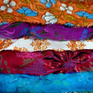 May include: A stack of colorful fabric scraps with floral patterns. The fabrics are in shades of orange, purple, white, red, and blue.