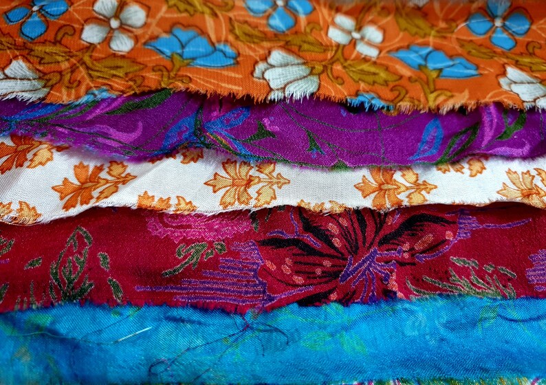 May include: A stack of colorful fabric scraps with floral patterns. The fabrics are in shades of orange, purple, white, red, and blue.