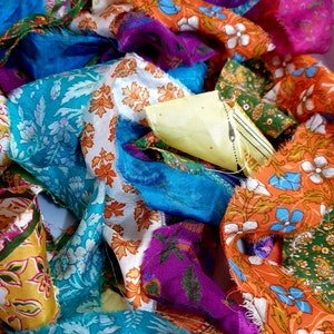 May include: A pile of colorful fabric scraps with floral patterns in shades of blue, orange, green, purple, and yellow. The fabric is silk and has a soft, flowing texture.