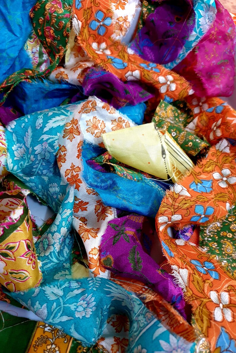 May include: A pile of colorful fabric scraps with floral patterns in shades of blue, orange, green, purple, and yellow. The fabric is silk and has a soft, flowing texture.
