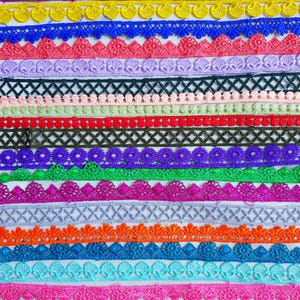 May include: A selection of colourful lace trims in various designs and widths. The trims feature scalloped edges, floral patterns, and geometric shapes. Colours include pink, yellow, blue, green, orange, and purple.