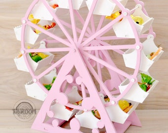 May include: Pink wooden Ferris wheel candy holder with white compartments. The Ferris wheel has 12 compartments and is decorated with white dots. The Ferris wheel is on a wooden base.