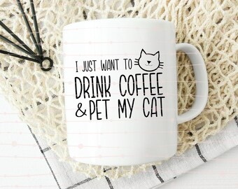 May include: White ceramic coffee mug with a black cat illustration and the text "I JUST WANT TO DRINK COFFEE & PET MY CAT." The mug has a curved handle and is sitting on a white and beige surface.