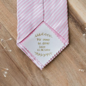 Może przedstawiać: Krawat w paski różowe i białe z przymocowaną białą metką. Metka zawiera złoty napis "Für immer an deiner Seite 22.06.2024".