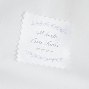 Puede incluir: Una etiqueta blanca con un borde festoneado y un diseño floral morado. El texto en la etiqueta dice "Ab heute Frau Fuchs 23.09.2019".