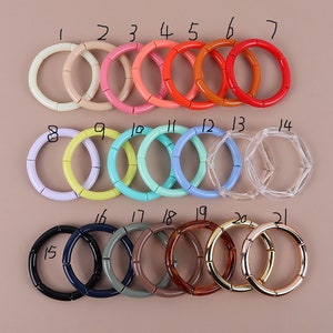 Könnte beinhalten: Einundzwanzig bunte Plastikarmbänder, nummeriert von 1 bis 21, in verschiedenen Farben, darunter Pink, Blau, Gelb, Grün, Rot, Orange, Schwarz, Braun und Gold.