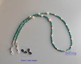Puede incluir: Cadena de gafas de cuentas verdes y doradas con detalles de perlas blancas. La cadena se muestra extendida con un par adicional de bucles negros. "SarahFindings" está escrito en la esquina inferior derecha de la imagen.