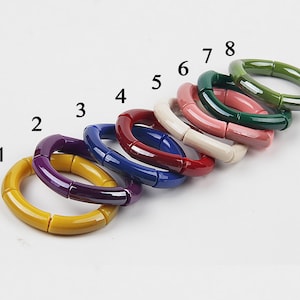 Puede incluir: Ocho pulseras rígidas de cerámica de colores con un diseño de bambú. Las pulseras están dispuestas en fila de amarillo a verde, con los números del 1 al 8 etiquetando cada pulsera.