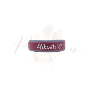 Puede incluir: Un collar para mascotas de color granate y gris con el nombre "Mikosh" y un s&iacute;mbolo de coraz&oacute;n grabado en blanco. El collar tiene forma rectangular con bordes redondeados. El fondo es blanco con una huella de pata.