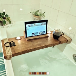 May include: Wooden bath tray with rope handles, a glass of red wine, a tablet, and a candle. The tray is placed over a bathtub filled with water.