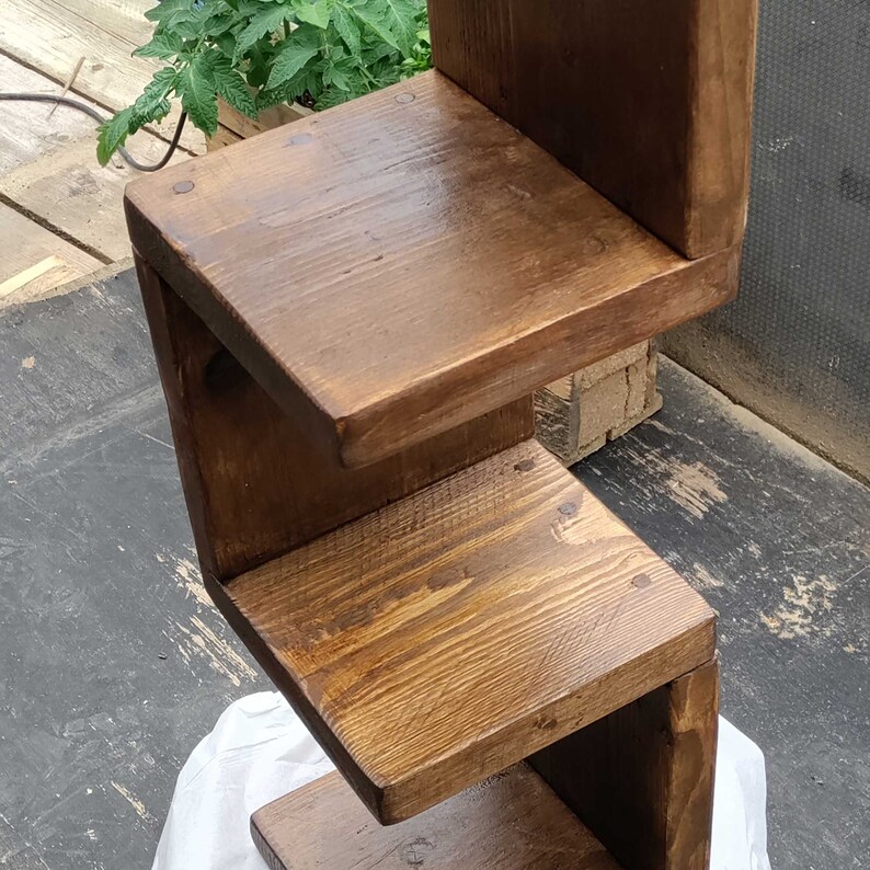 May include: A wooden shelf unit with three shelves. The shelves are made of dark brown wood and have a natural finish. The shelves are stacked on top of each other in a staggered pattern.