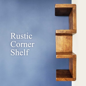 May include: Rustic Corner Shelf, a wooden shelf unit with three shelves, mounted on a blue wall. The shelf is made of stained wood and has a rustic look.