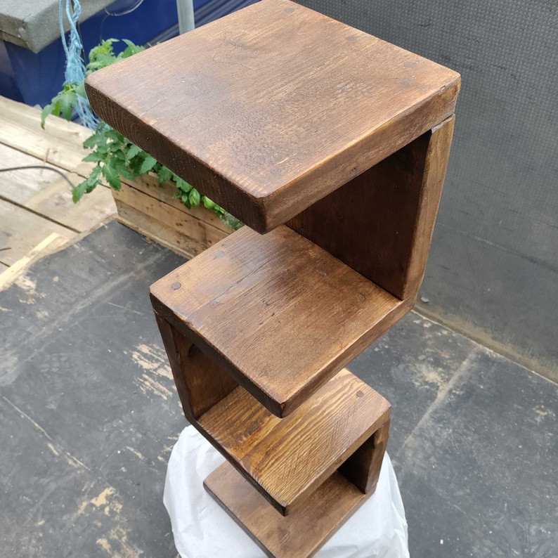 May include: A dark brown wooden shelf unit with three shelves. The shelves are stacked in a staggered pattern, creating a unique and modern design.
