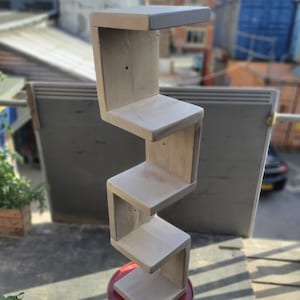 May include: White wooden shelf unit with five shelves, each shelf is angled and staggered, creating a unique zig-zag design. The shelf unit is freestanding and appears to be made from reclaimed wood.