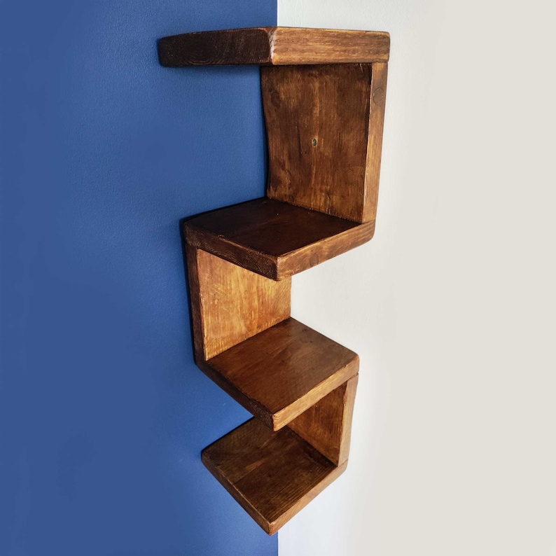 May include: A wooden wall shelf with four shelves in a staggered design. The shelves are stained a dark brown color and are mounted on a blue wall.