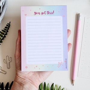 May include: A pastel pink and blue notepad with a rainbow gradient and white lines. The notepad has the text "you got this!" in pink lettering and a pink heart at the bottom.