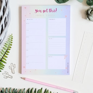 May include: A pastel pink and blue weekly planner notepad with the text "You got this! Inhale Exhale" at the top. The notepad has a rainbow gradient background with white polka dots and a pink heart in the bottom right corner.