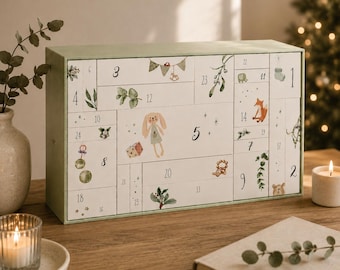 Può includere: Un calendario dell'avvento rettangolare con cornice verde chiaro e cassetti bianchi numerati da 1 a 24. La superficie frontale è decorata con illustrazioni ad acquerello di un coniglio, una volpe, un orso, fogliame e stelle.
