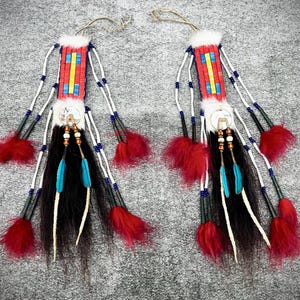 Puede incluir: Dos accesorios para el cabello de estilo nativo americano. Cada uno presenta una sección de cuentas rojas, amarillas y azules, piel blanca, cabello negro, plumas turquesas y acentos rojos esponjosos. Hebras de cuentas blancas y un lazo completan el diseño.