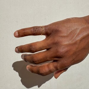 May include: A gold ring with a simple, curved design. The ring is worn on the index finger of a hand.