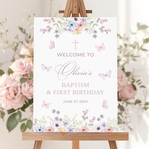 Puede incluir: Un letrero blanco sobre un caballete de madera con detalles florales y mariposas. El letrero dice "Bienvenida al Bautizo y Primer Cumpleaños de Olivia" con una cruz y la fecha 27 de junio de 20XX.