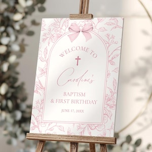 Puede incluir: Un letrero de bienvenida rosa y blanco sobre un caballete de madera. El letrero dice "Bienvenida a Caroline's Bautizo y Primer Cumpleaños" con detalles florales y de lazo. El letrero se muestra en interiores.
