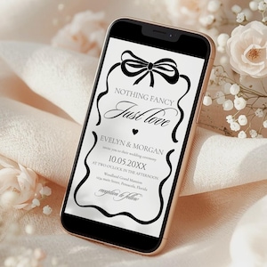 May include: A smartphone displays a wedding invitation with the text "NOTHING FANCY Just love" in elegant script. The invitation includes the names Evelyn & Morgan, the date 10.05.20XX, and reception details. The phone is set against a soft, neutral background with floral accents.